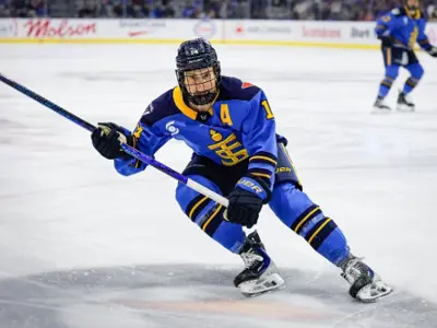 Hockey player in blue uniform skates low to the ice while controlling the puck during a game.