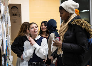 Students speak with a staff member while looking at a display of student work on a bulletin board.