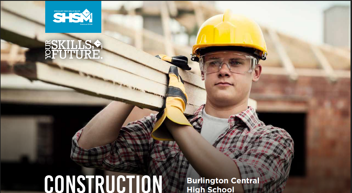 a student wearing a yellow hard hat, yellow protective gloves and safety goggles carrying lumber over their shoulder.