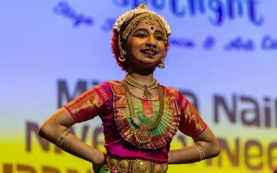 Student performs a traditional dance on stage wearing colourful cultural attire and ornate jewelry during a student showcase event.